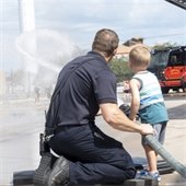 A Firefighter helps a young child spray water at the Fire Station.